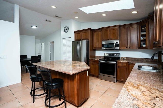 kitchen featuring appliances with stainless steel finishes, a sink, a skylight, lofted ceiling, and a kitchen island