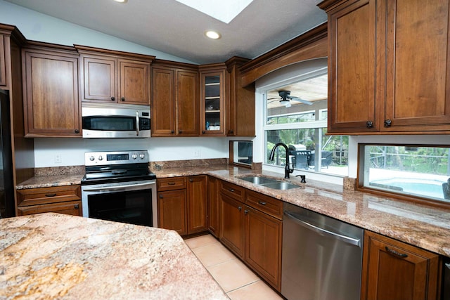 kitchen featuring appliances with stainless steel finishes, a sink, vaulted ceiling, a skylight, and light stone countertops