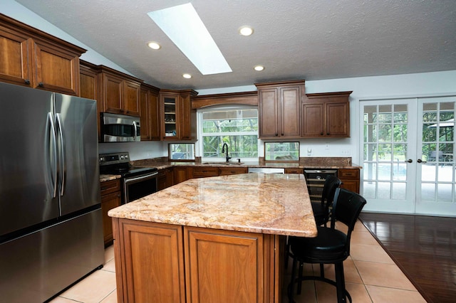 kitchen with stainless steel appliances, a sink, a skylight, light tile patterned floors, and a kitchen island