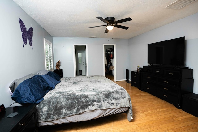 bedroom featuring light wood-style flooring, a spacious closet, a closet, a textured ceiling, and ceiling fan