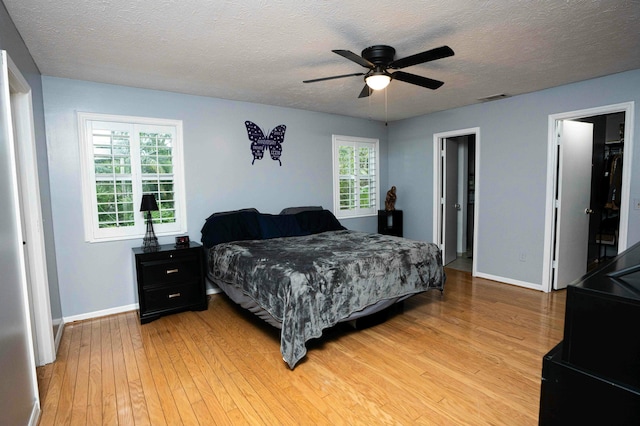 bedroom featuring light wood finished floors, baseboards, a textured ceiling, and ceiling fan
