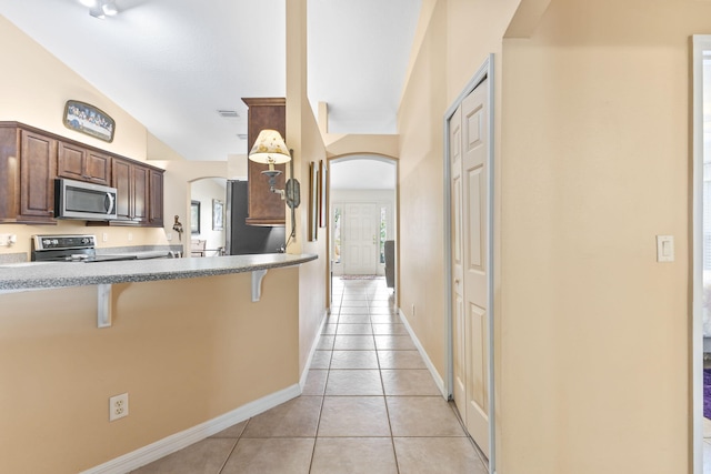 kitchen with light tile patterned floors, a kitchen bar, arched walkways, and stainless steel appliances