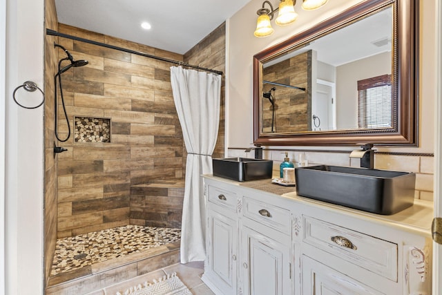 bathroom with double vanity, visible vents, a tile shower, and a sink