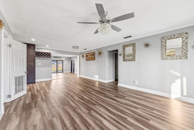 unfurnished living room with crown molding, visible vents, a ceiling fan, wood finished floors, and baseboards