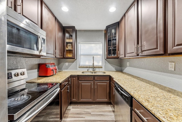 kitchen featuring stainless steel appliances, a sink, a textured ceiling, and light stone countertops