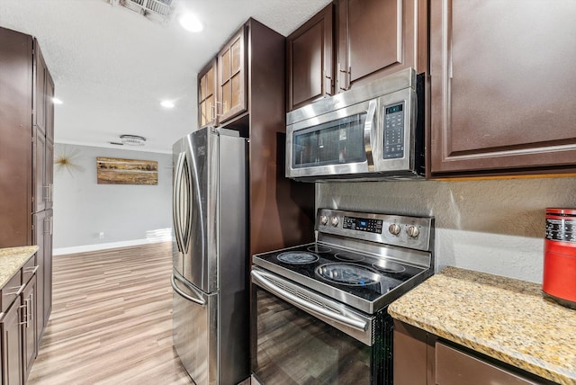 kitchen featuring stainless steel appliances, visible vents, light wood-style floors, light stone countertops, and baseboards