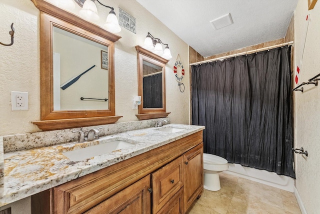 bathroom featuring a textured wall, double vanity, a sink, and toilet