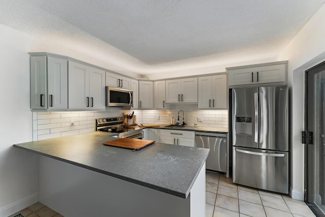 kitchen featuring a peninsula, a sink, appliances with stainless steel finishes, tasteful backsplash, and dark countertops