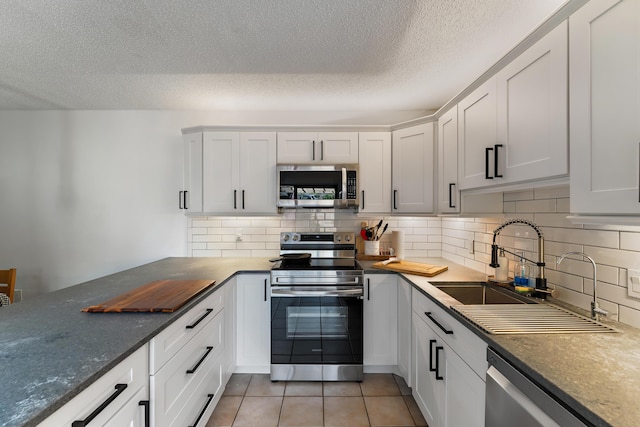 kitchen with light tile patterned floors, tasteful backsplash, white cabinets, appliances with stainless steel finishes, and a sink