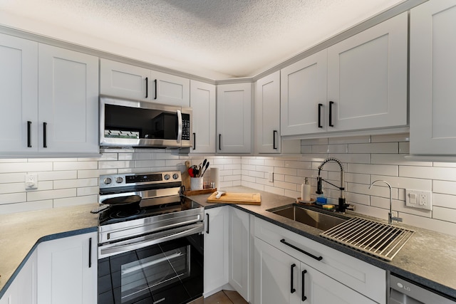 kitchen featuring a textured ceiling, decorative backsplash, stainless steel appliances, and a sink