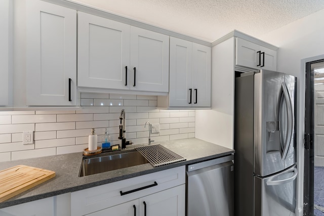 kitchen with appliances with stainless steel finishes, a sink, a textured ceiling, and decorative backsplash