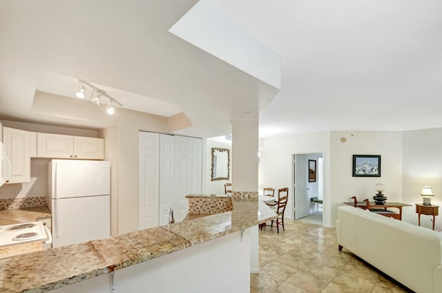 kitchen featuring open floor plan, freestanding refrigerator, a peninsula, light stone countertops, and stove