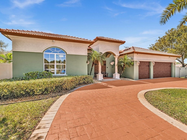 mediterranean / spanish house featuring an attached garage, fence, a tiled roof, stucco siding, and driveway