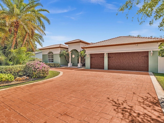 mediterranean / spanish home with a tile roof, decorative driveway, an attached garage, and stucco siding