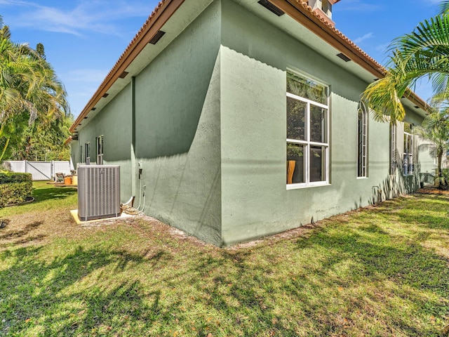 view of side of property featuring fence, a tile roof, stucco siding, cooling unit, and a yard