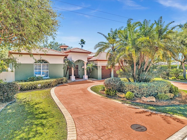 mediterranean / spanish-style home featuring a tile roof, decorative driveway, a front lawn, and stucco siding