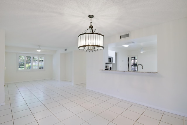 unfurnished room featuring visible vents, light tile patterned flooring, a textured ceiling, a sink, and ceiling fan with notable chandelier