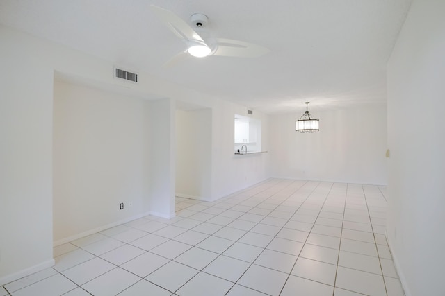 empty room with light tile patterned floors, visible vents, baseboards, and ceiling fan with notable chandelier