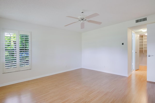 unfurnished room featuring light wood-style floors, baseboards, visible vents, and ceiling fan