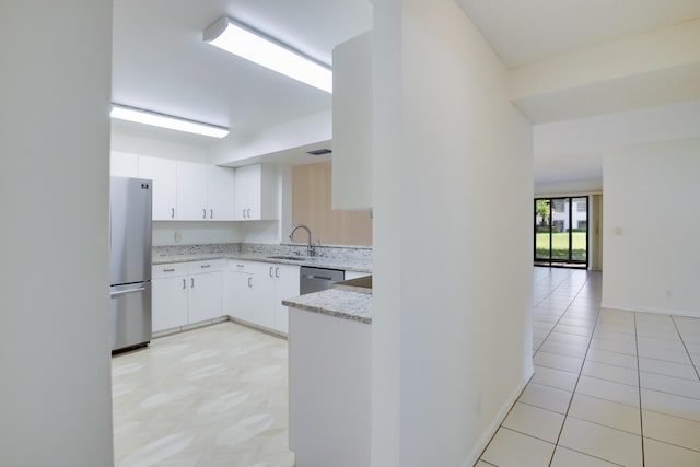 kitchen featuring light tile patterned floors, a sink, white cabinets, appliances with stainless steel finishes, and light stone countertops