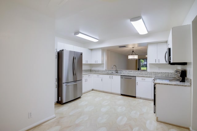 kitchen featuring light stone counters, stainless steel appliances, hanging light fixtures, white cabinetry, and a sink