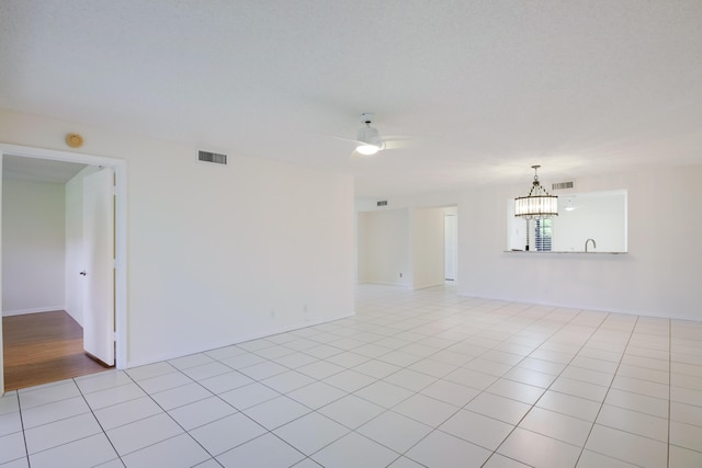 spare room featuring light tile patterned floors, visible vents, and ceiling fan with notable chandelier