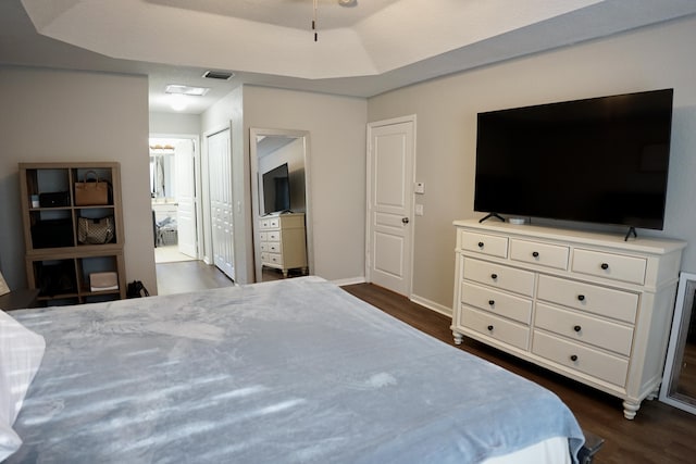 bedroom featuring connected bathroom, visible vents, baseboards, dark wood-style floors, and a raised ceiling