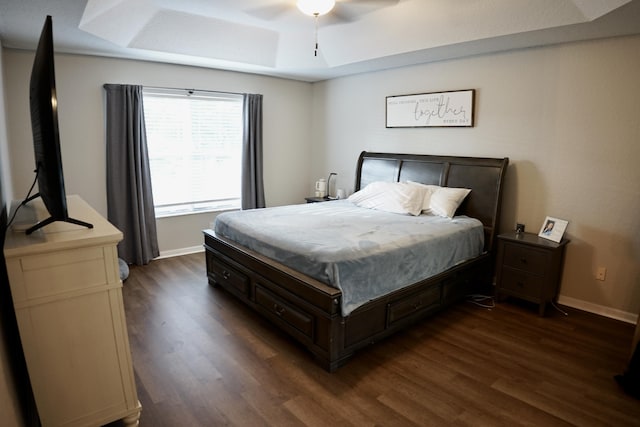 bedroom with dark wood-style floors, a raised ceiling, ceiling fan, and baseboards