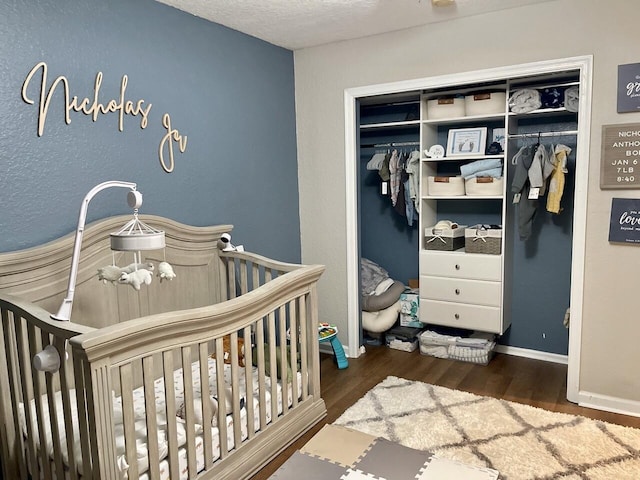 bedroom featuring a textured ceiling, wood finished floors, baseboards, a closet, and a nursery area