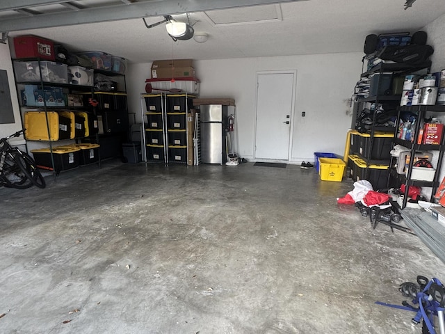 garage with a garage door opener, freestanding refrigerator, and electric panel