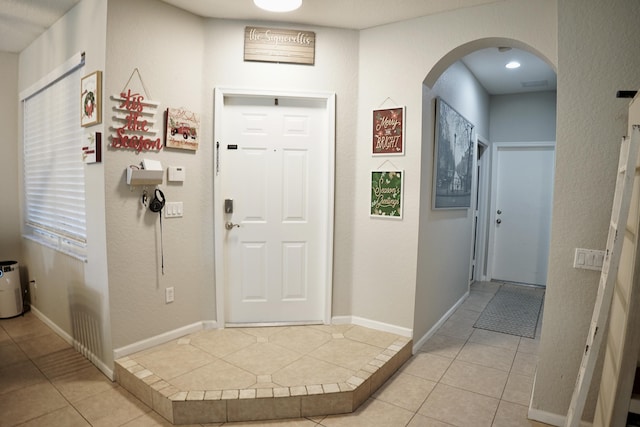 foyer with arched walkways, light tile patterned flooring, and baseboards