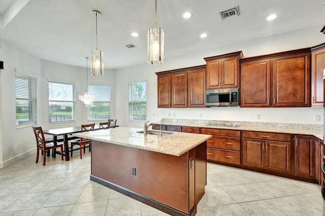 kitchen with light stone counters, light tile patterned floors, stainless steel microwave, visible vents, and a sink