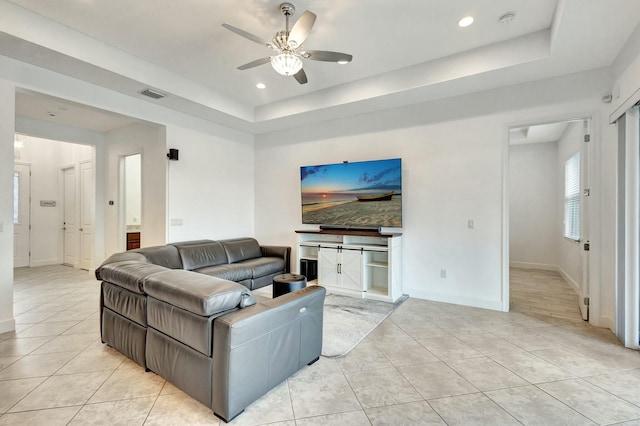 living area featuring light tile patterned floors, a tray ceiling, visible vents, and baseboards