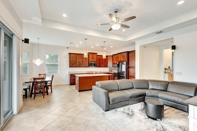 living room with a tray ceiling, light tile patterned floors, recessed lighting, visible vents, and ceiling fan with notable chandelier