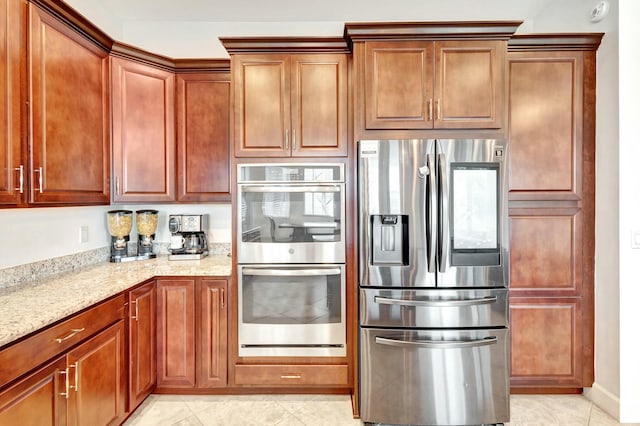 kitchen featuring light stone countertops, light tile patterned floors, appliances with stainless steel finishes, and brown cabinetry