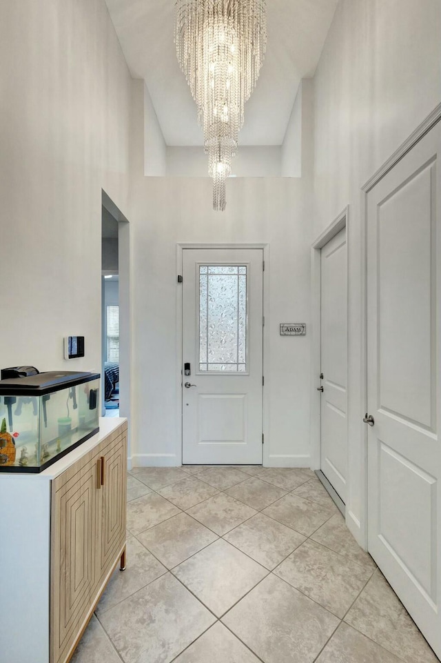 foyer entrance featuring a high ceiling, light tile patterned floors, baseboards, and an inviting chandelier