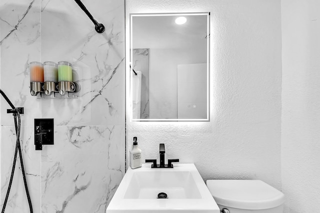 full bathroom with a textured wall, a marble finish shower, a sink, and toilet