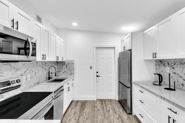 kitchen featuring light stone counters, stainless steel appliances, light wood-style floors, white cabinetry, and a sink