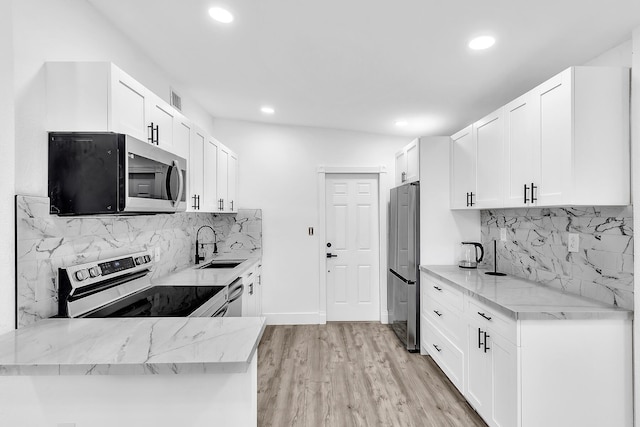 kitchen featuring light wood finished floors, stainless steel appliances, white cabinets, a sink, and light stone countertops