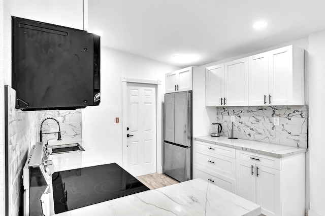 kitchen with tasteful backsplash, white cabinetry, freestanding refrigerator, and light stone countertops