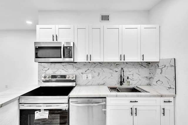 kitchen featuring stainless steel appliances, a sink, visible vents, white cabinets, and tasteful backsplash