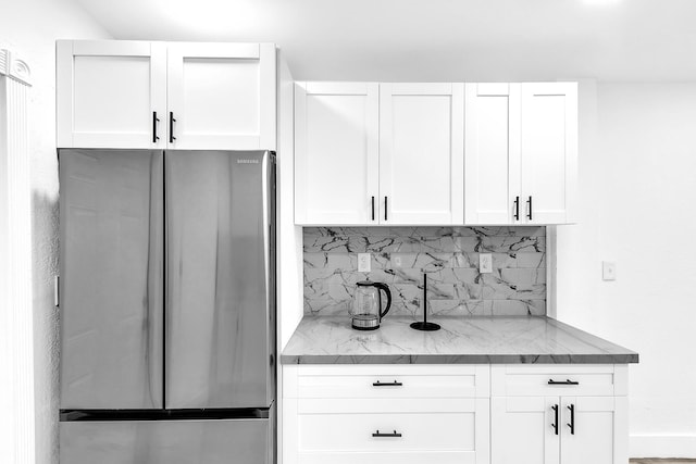 kitchen with light stone counters, white cabinets, backsplash, and freestanding refrigerator