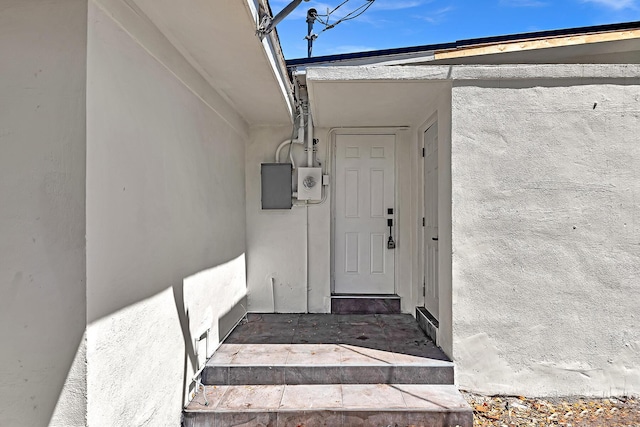 entrance to property with electric panel and stucco siding