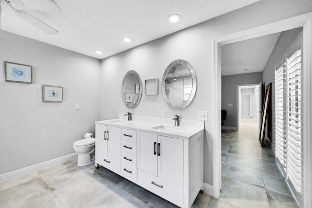 bathroom with double vanity, toilet, baseboards, and a sink