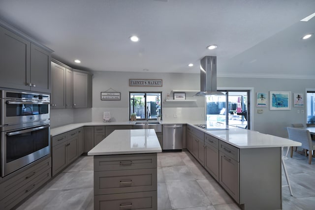 kitchen featuring gray cabinets, island exhaust hood, appliances with stainless steel finishes, a peninsula, and light countertops