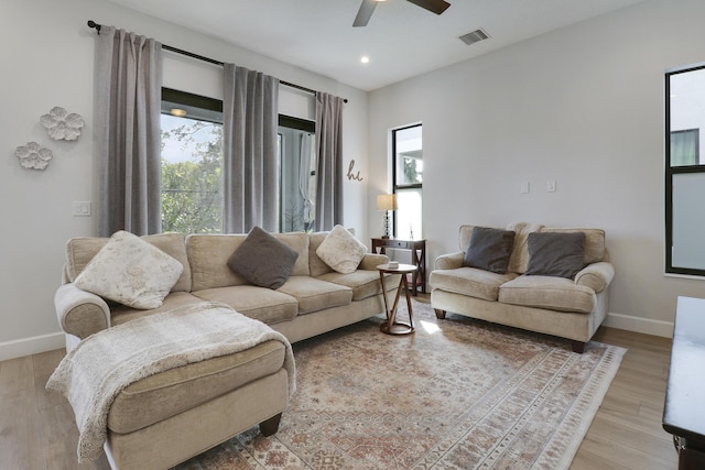 living room featuring light wood-type flooring, baseboards, visible vents, and a ceiling fan