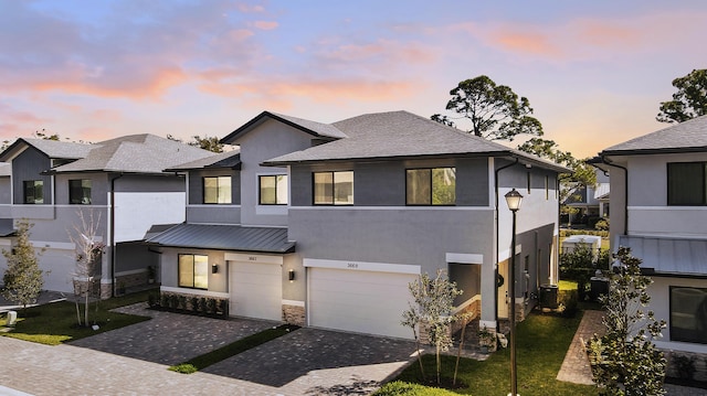 view of front of home with metal roof, a garage, stone siding, decorative driveway, and stucco siding