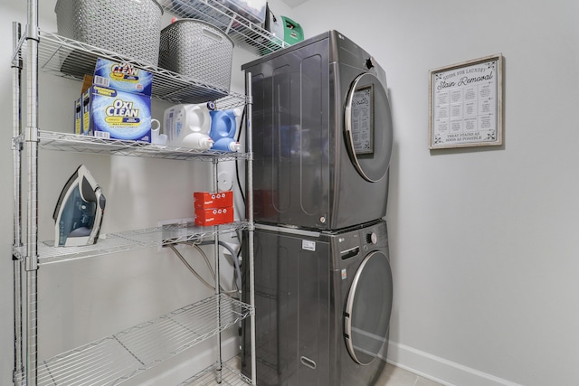 clothes washing area featuring stacked washing maching and dryer, baseboards, laundry area, and tile patterned floors