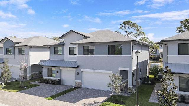 view of front of property featuring decorative driveway, stucco siding, central AC, metal roof, and a garage