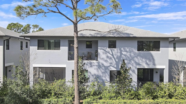 rear view of house with a shingled roof, fence, and stucco siding